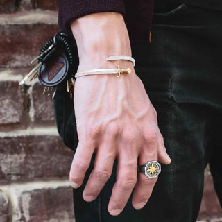 Hand wearing silver bracelet and ring with compass design against a brick wall.