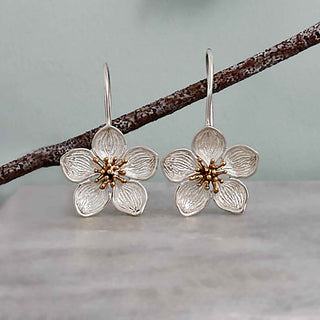 Silver flower-shaped earrings with gold centers on a branch against a light background