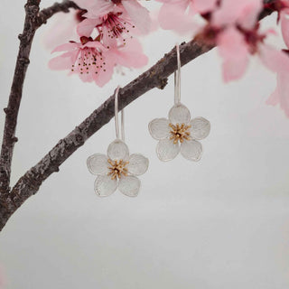 Floral earrings hanging from a branch with pink blossoms.