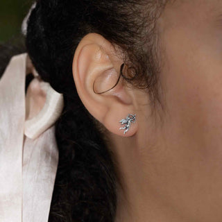 Close-up of an ear wearing a silver cupid stud earring with blurred background.