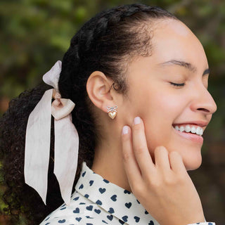 Woman wearing a gold earring with a bow and heart design, smiling outdoors.
