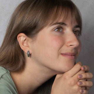 Close-up of a woman wearing fern huggie hoop earrings with a neutral background