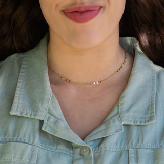 A close-up of a model wearing a delicate gold chain necklace, styled with a light blue denim shirt.