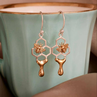 Gold bee-themed earrings displayed on a teal mug with a brown background
