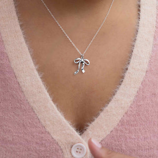 Silver necklace with a bow pendant worn by a person in a pink cardigan.