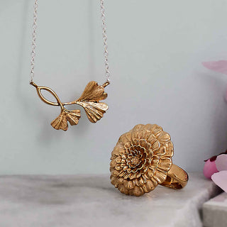 Gold necklace and ring on a light gray surface with a soft pink background