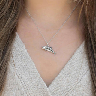 Silver fish pendant necklace worn by a person with brown hair and a beige sweater.