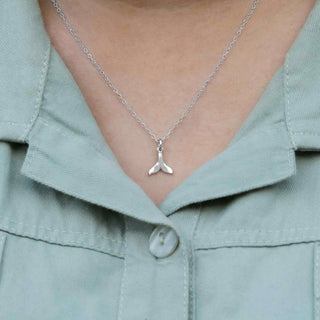 Silver necklace with a whale tail pendant worn by a person in a light green shirt.