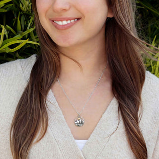 Woman wearing a silver necklace with a pendant outdoors