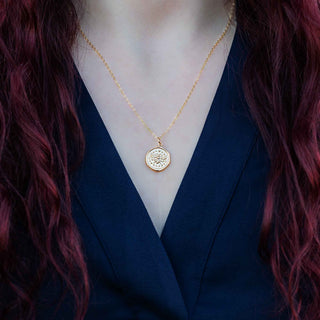 Person wearing a gold necklace with a coin pendant, dressed in a blue outfit.