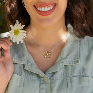 Woman wearing a silver necklace with a flower pendant, holding a white flower.