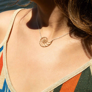 Close-up of a necklace with a shell pendant worn by a person against a blurred natural background