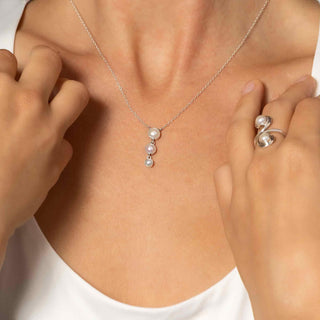 Triple Pearl Drop Necklace and Pearl ring on a person wearing a white shirt