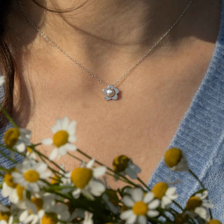 Person wearing a necklace with a flower pendant, surrounded by daisies.