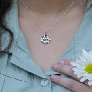 Person wearing a silver necklace with a pendant, holding a white flower.