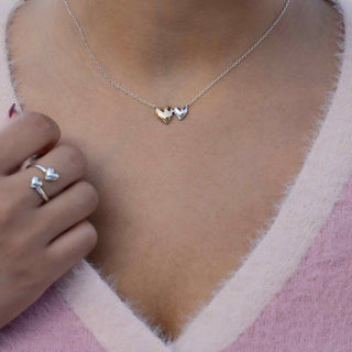 Necklace with heart pendants worn by a person, with matching rings on a pink fabric background.