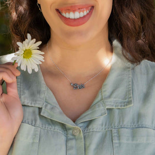Woman wearing a necklace with a small pendant, holding a white flower.
