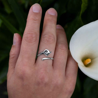Hand wearing a silver ring with a white flower in the background