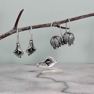 Silver floral earrings and ring on a branch with a gray background