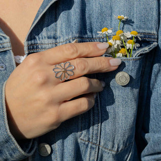 Hand wearing a silver flower ring with denim jacket and buttoned pocket containing flowers