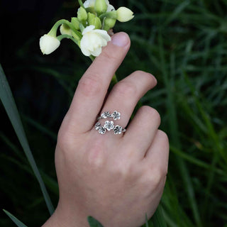Hand wearing a silver ring with floral design holding a small white flower against a green background