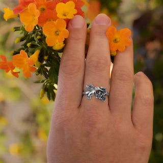 Hand wearing a silver ring with a dragon design, held against a background of orange flowers.