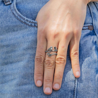A close-up of a hand wearing a silver bird wrap ring, resting on blue denim jeans.