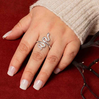 Hand wearing a silver snake-shaped ring on a red background
