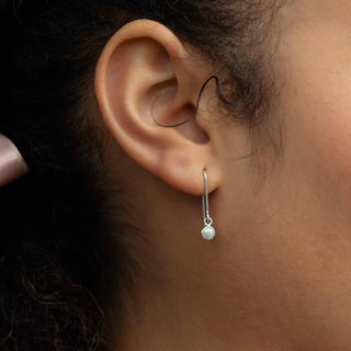 Close-up of an ear wearing a silver earring with a pearl drop.