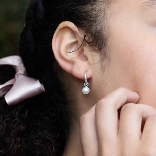 Close-up of an ear wearing a silver earring with a pearl, with a blurred background.