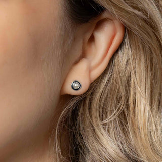 Close-up of an ear wearing a small stud earring with blonde hair.