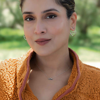Woman wearing hoop earrings and a necklace with a blurred green background