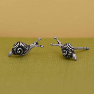 Pair of silver snail-shaped earrings on a green surface with a beige background