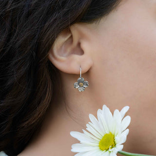 Close-up of a woman's ear wearing a silver flower earring with a white daisy in the foreground.