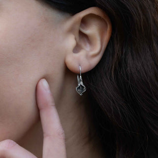 Close-up of an ear wearing a silver earring with a dark gemstone, with a finger pointing to it.