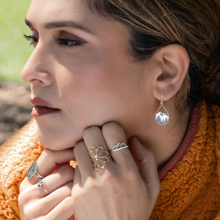 Close-up of a woman wearing silver earrings and rings with an orange sweater.