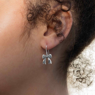 Bow dangle earrings close up on model with dark hair. 