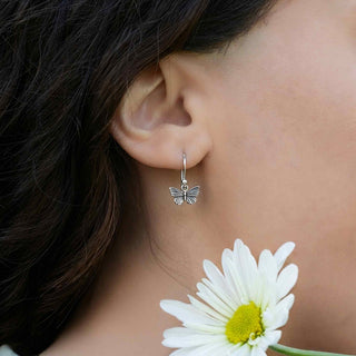 Butterfly earring worn by a person with a white flower in the foreground