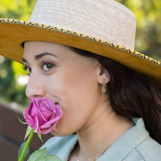 Woman wearing a wide-brimmed hat with a pink rose in her mouth, outdoors.