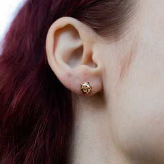 Gold stud earring worn on a person's ear with a blurred background