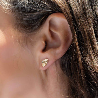 Close-up of an ear wearing a gold earring with a blurred background