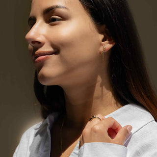 Close-up of a woman wearing Bronze Crossed Pods Post Earrings and a ring, with a neutral background