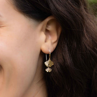 Bronze ginkgo leaf-shaped earring worn by a person with dark hair.