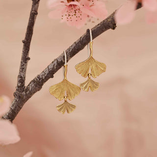 Bronze leaf-shaped earrings on a branch with pink blossoms