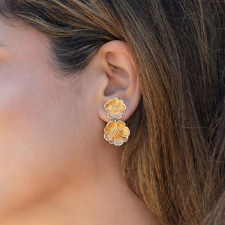 Close-up of a person wearing bronze floral earrings with blurred background