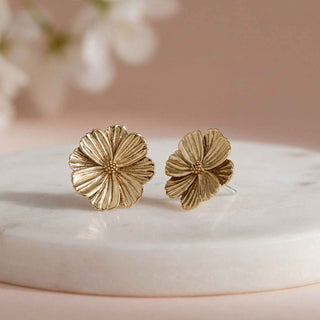 Gold floral earrings on a marble surface with a soft pink background