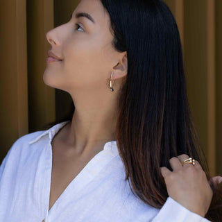 Woman wearing Bronze Long Teardrop Hook Earrings and a ring, with a blurred background