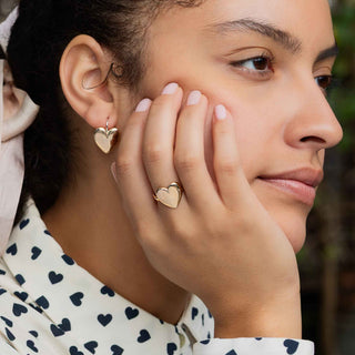 Woman wearing heart-shaped earrings and a ring, with a blurred background
