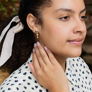 Woman wearing Cascading Hearts stud earrings with a blurred background