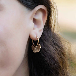 Close-up of an ear wearing a bronze earring with a blurred natural background
